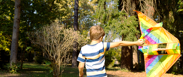 Child in striped shirt running with a colourful kite in a park setting
