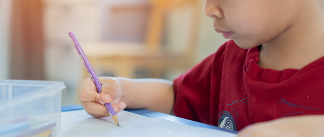 Young child concentrating while writing or drawing with a purple pencil at a table