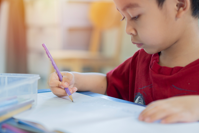 Young child concentrating while writing or drawing with a purple pencil at a table